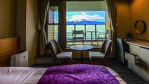 A hotel room with a bed, a desk, two chairs, and a view of a mountain through a window. - The Noborisaka Hotel (Fujikawaguchiko)