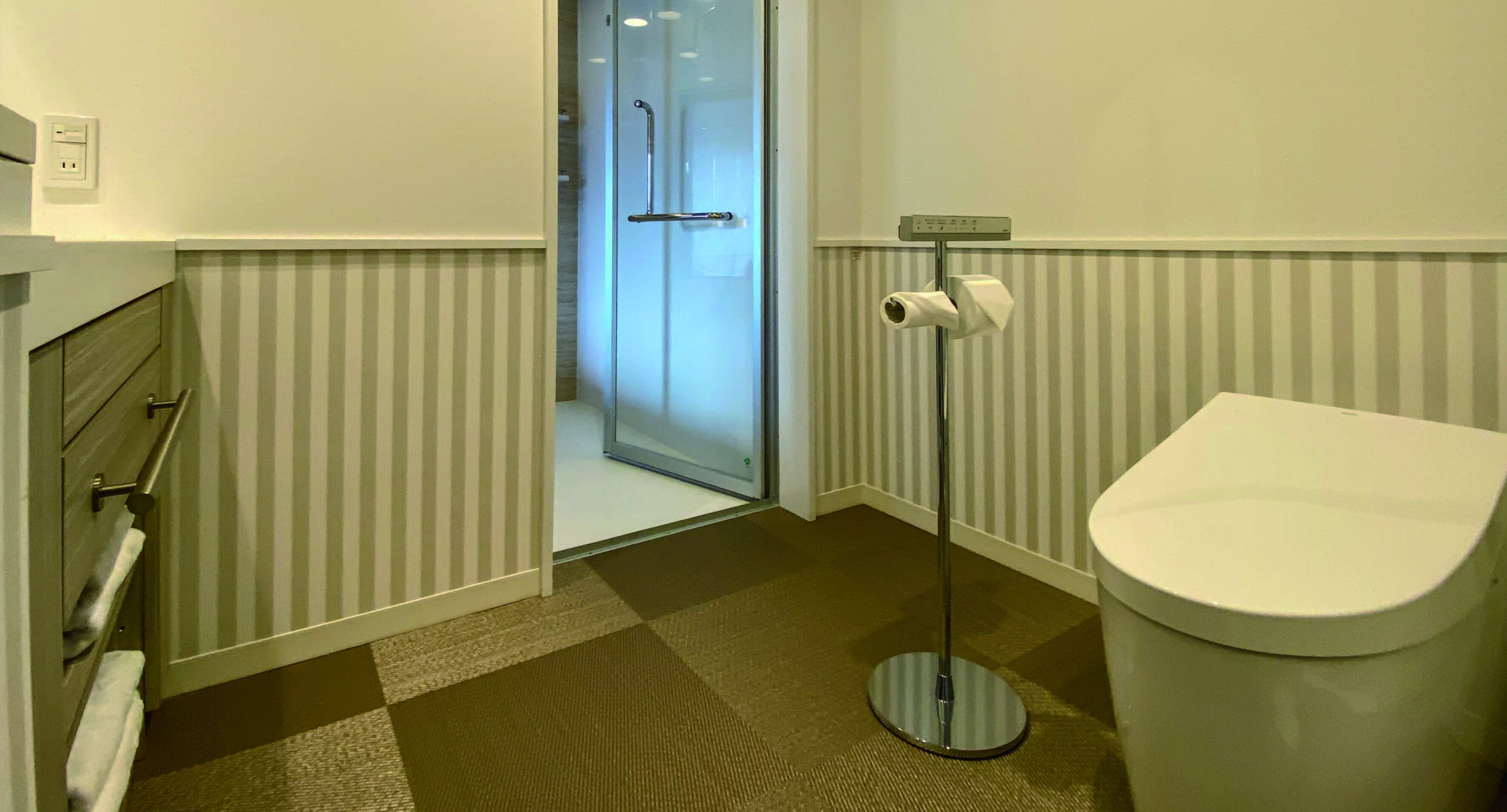 A bathroom with a toilet, a towel rack, a glass shower door, and a toilet paper holder.