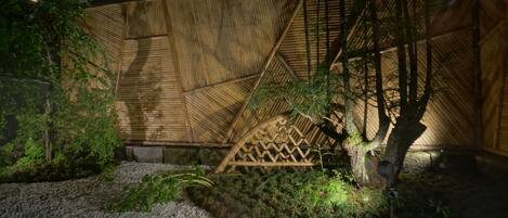 Estructura de bambú con diseño de celosía de madera, rodeada de vegetación y grava.