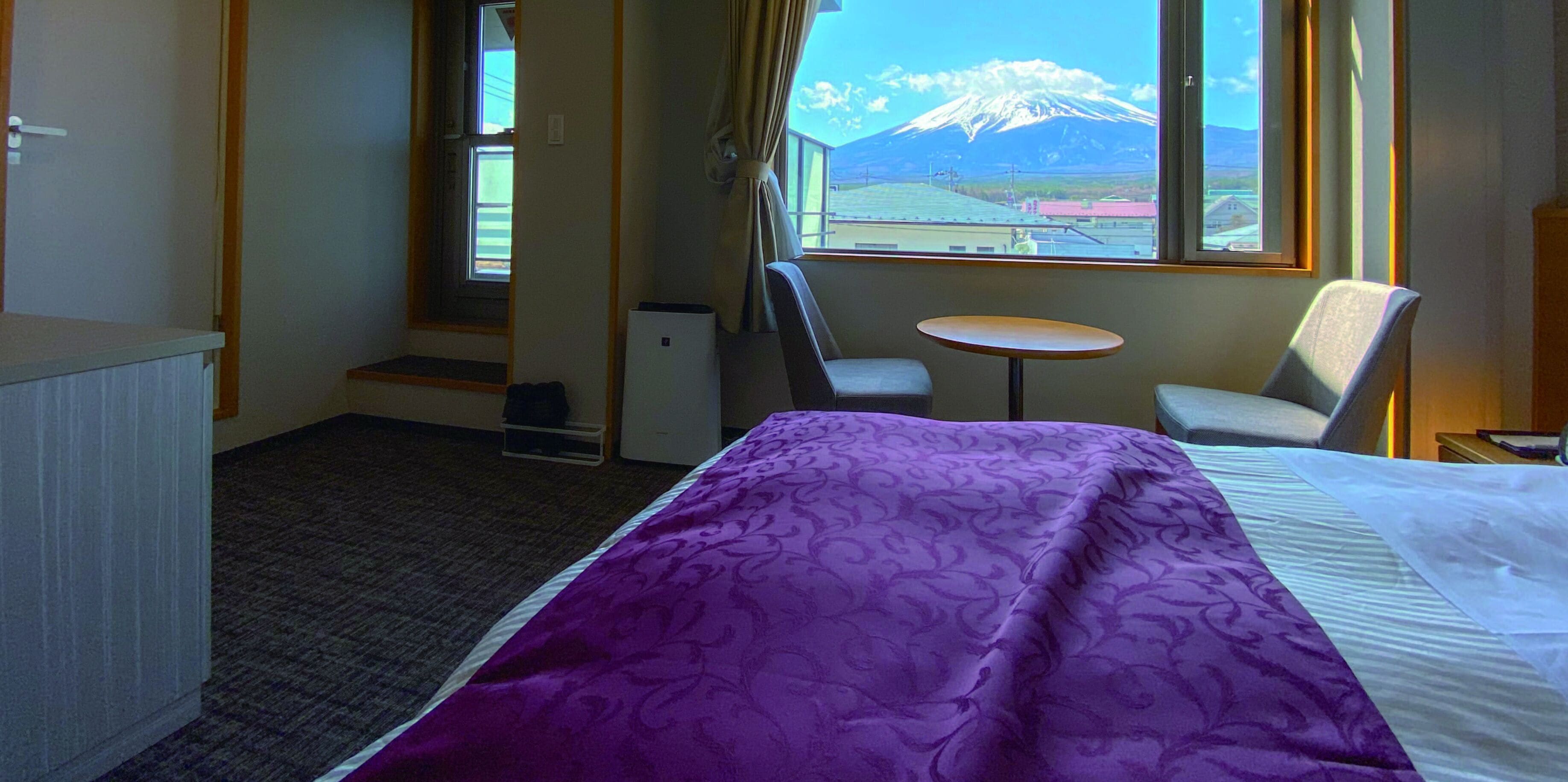 A hotel room with a bed, a small table, two chairs, a desk, and a view of a mountain.