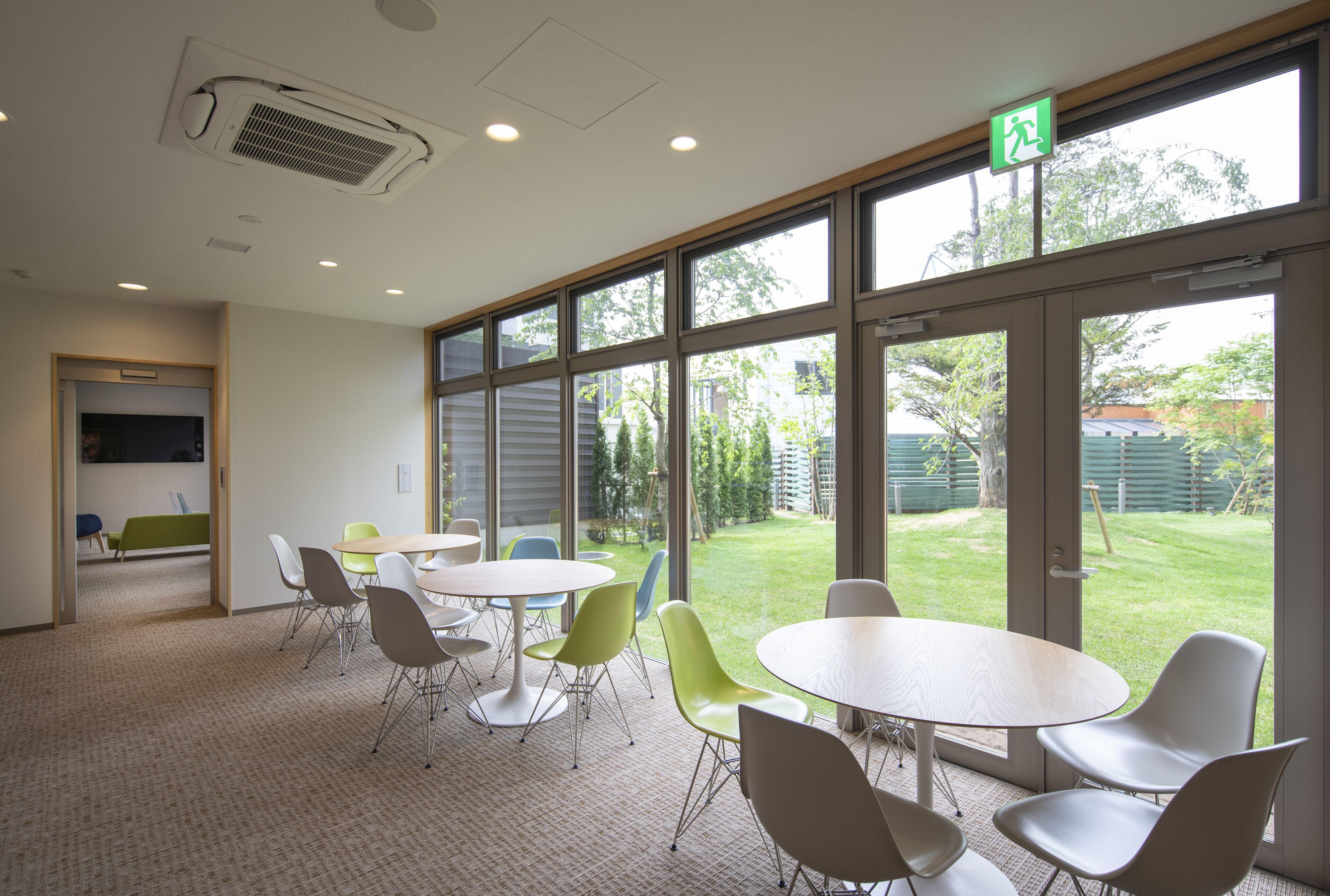 A conference room with large windows, a fire extinguisher, and a green exit sign.