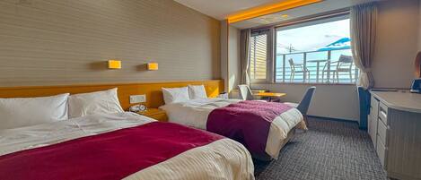 A hotel room with two beds, a desk, a chair, and a view of the sea.