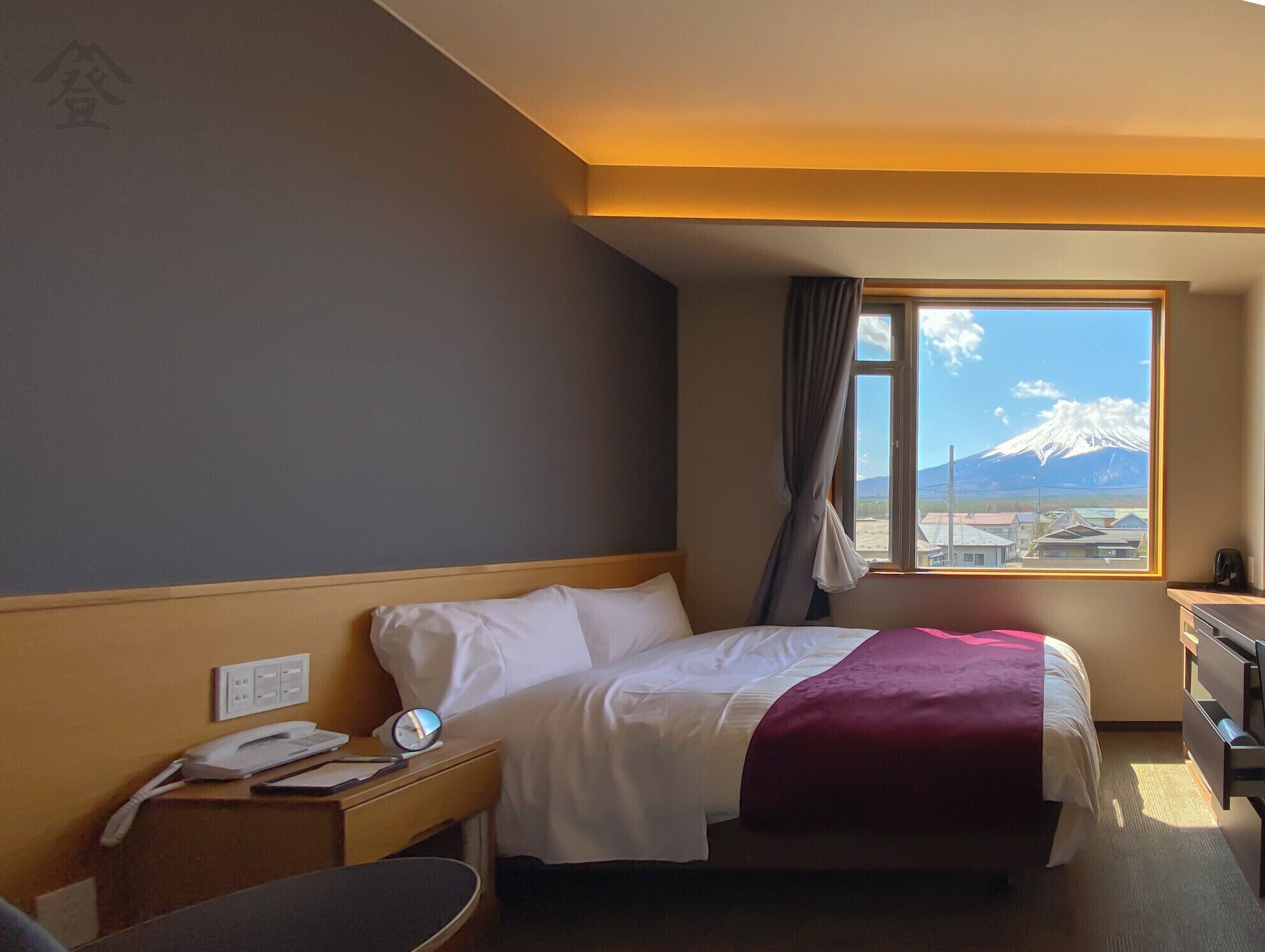 Habitación de hotel con cama, mesita de noche y ventana con vista a la montaña.