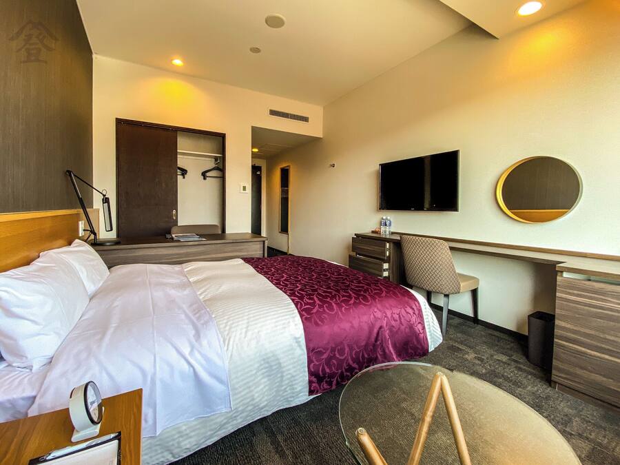Een hotelkamer met een bed, bureau, stoel, televisie en een spiegel.