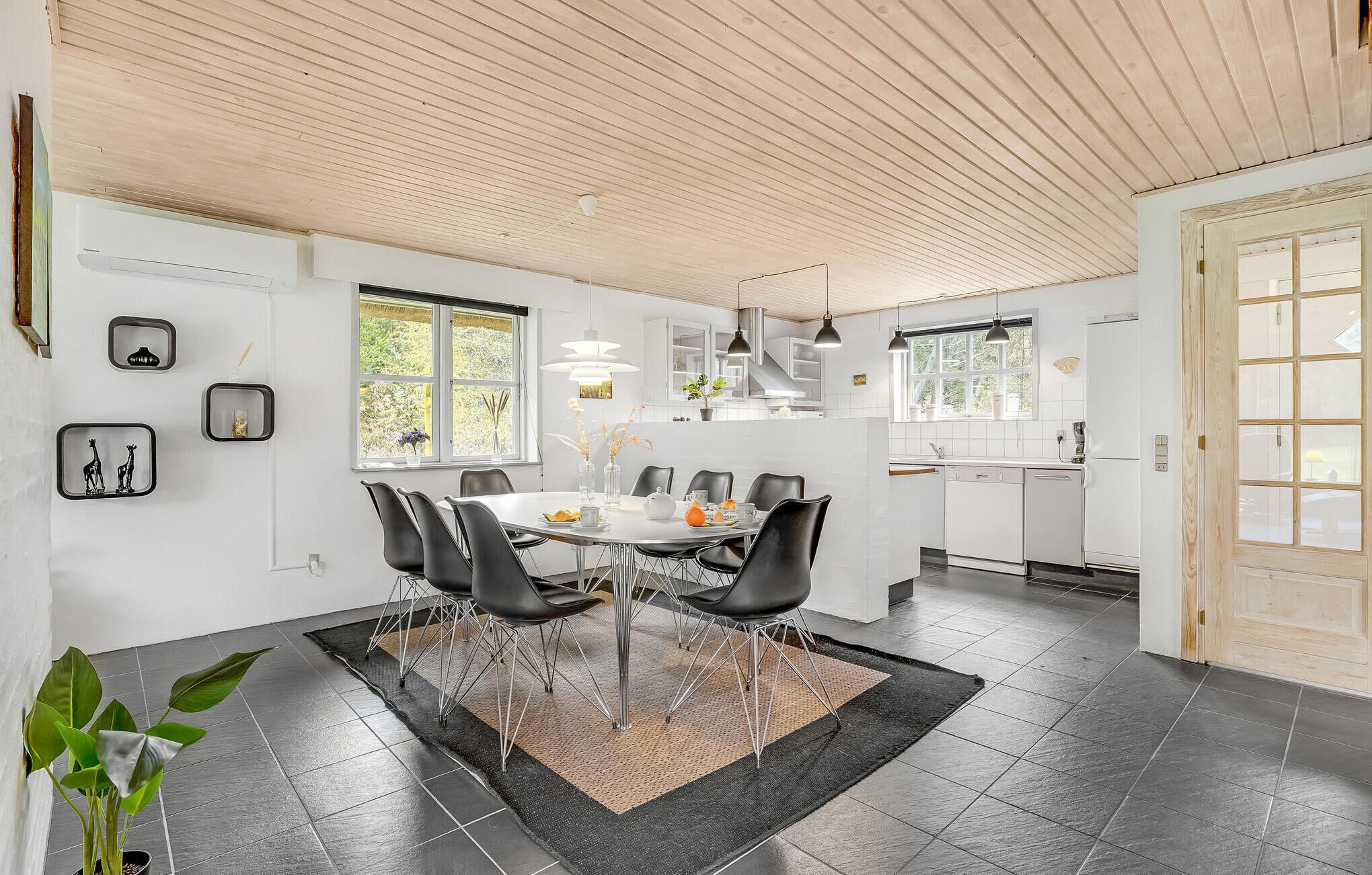 A modern kitchen with white cabinets, a dining area with a round table and black chairs, and a wooden ceiling.