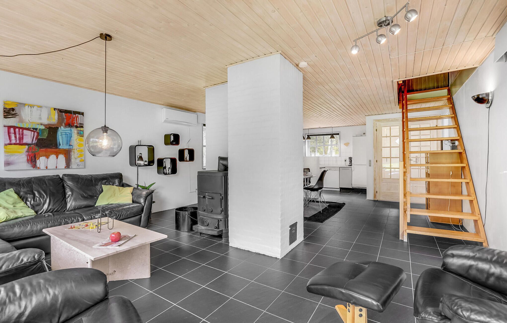 A modern living room with a black leather sofa, a coffee table, and a fireplace. There is a staircase leading to an upper level.