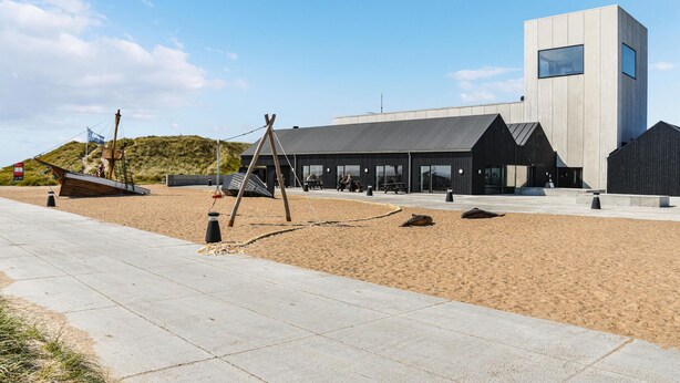A modern building with a flat roof and large windows, situated on a sandy beach with a concrete walkway in front. - Amazing home in Ulfborg with kitchen (Ulfborg)