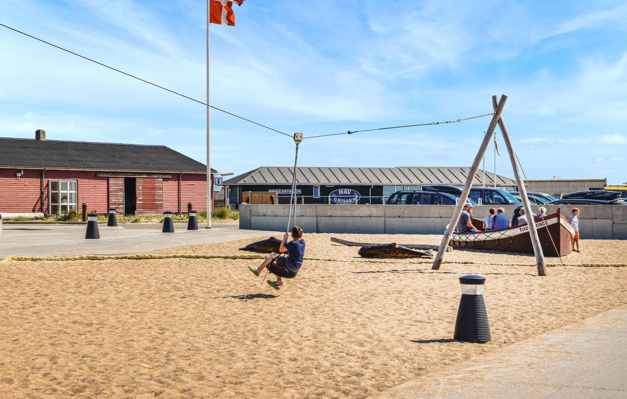 En sandstrand med et gyngestativ, en rød bygning og et skilt med teksten 'Hav Griljen'.