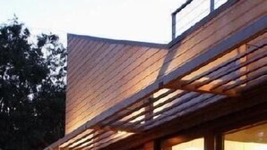 Une maison moderne dotée d’une terrasse en bois, de grandes baies vitrées et d’un balcon.