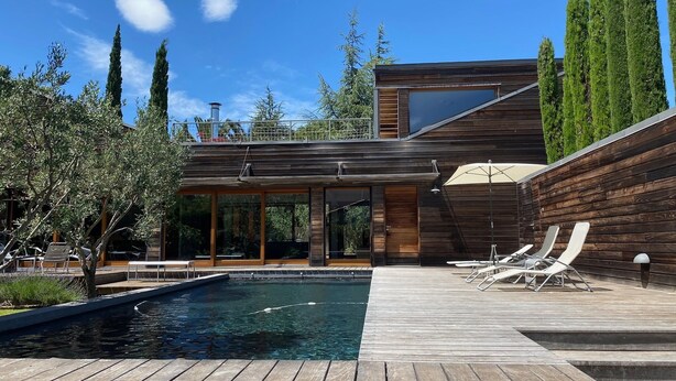 Une maison moderne dotée d’une terrasse en bois, d’une piscine et d’un espace salon extérieur.