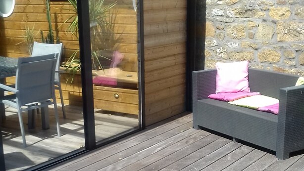 A wooden deck with a glass sliding door leading to a room with a wooden wall and a stone wall. - Penty for rent in a small village typical of the peninsula (crozon)