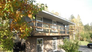 Un bâtiment à deux étages doté d’un balcon, d’une façade en briques et d’un petit porche à l’avant avec un banc.