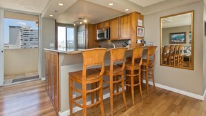 Una cocina moderna con armarios de madera, un refrigerador de acero inoxidable y un microondas. Hay tres taburetes de bar de madera y un espejo grande en la pared.