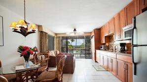 A modern kitchen with wooden cabinets, a refrigerator, and a dining area with wicker furniture and a glass table. - Your Perfect Beachfront Condo in Paradise - Sapphire Beach - Corner Unit (St Thomas)