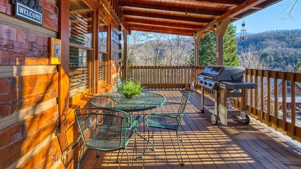 Eine Holzterrasse mit überdachter Sitzgelegenheit, Grill und Blick auf die umliegende Landschaft.