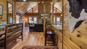 Ein Holzblockhaus-Interieur mit einer Holzbänkl, einem Esstisch, einem Kamin und einem Fellteppich.