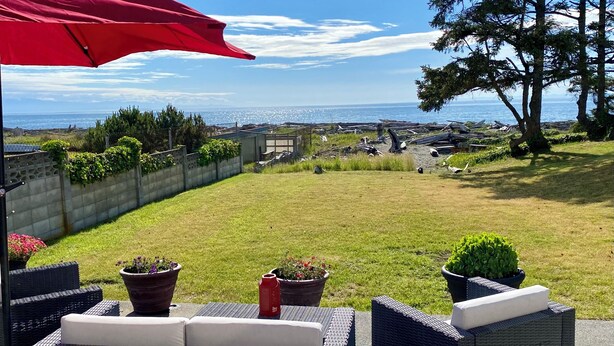 Een terras met rieten meubilair, plantenpotten en een rode parasol.