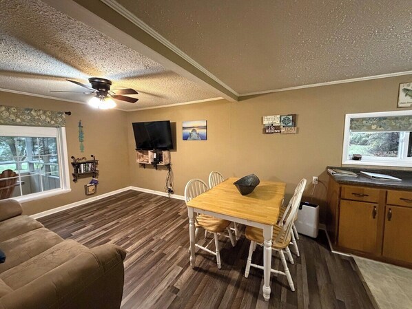 A dining area with a wooden table and chairs, a ceiling fan, and a television mounted on the wall. - Lakeside Cottage - Lake, Private Hot Tub (Guild)