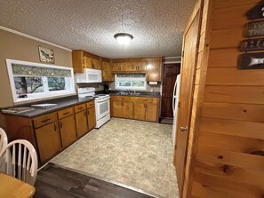 A compact kitchen with wooden cabinets, a white microwave, a stove, and a sink. - Lakeside Cottage - Lake, Private Hot Tub (Guild)