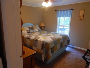 Une chambre à coucher comprenant un lit, une table de chevet, une lampe, une fenêtre avec vue et un ventilateur de plafond.