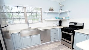 Een moderne keuken met roestvrijstalen apparatuur, lichtblauwe kastjes en een raam met zonwering.