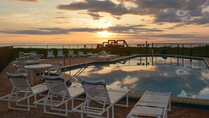 Una piscina con sillones de descanso, una terraza y vistas al atardecer sobre el agua.