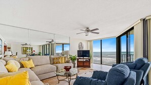 Una sala de estar moderna con sofá, sillones, televisor y un amplio ventanal con vista a la playa.