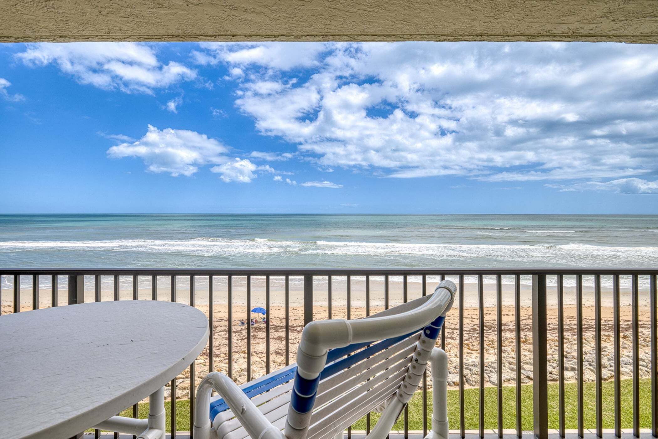 Ein Balkon mit Blick auf Strand und Meer, inklusive Tisch und Stuhl.
