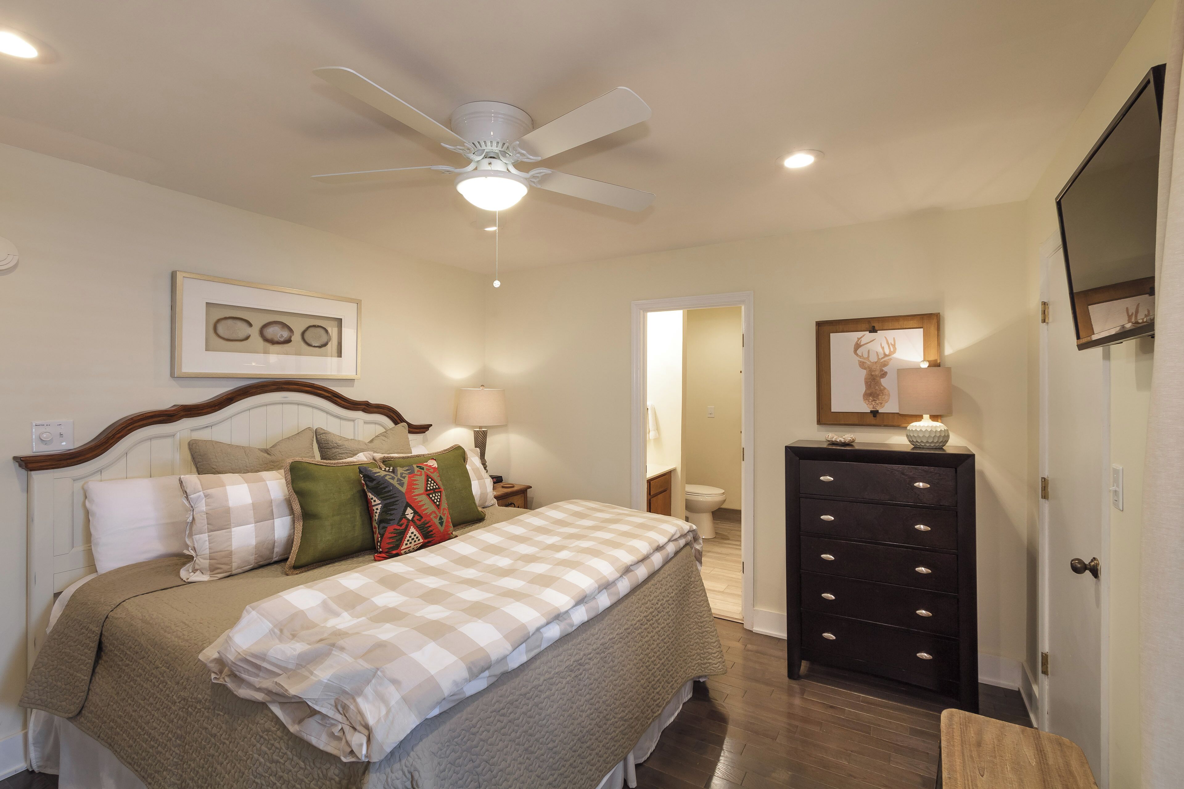 A bedroom with a bed, bedside lamps, a dresser, and a ceiling fan.