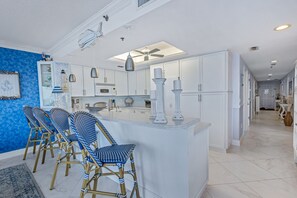 A kitchen with white cabinets, a central island, and blue chairs.