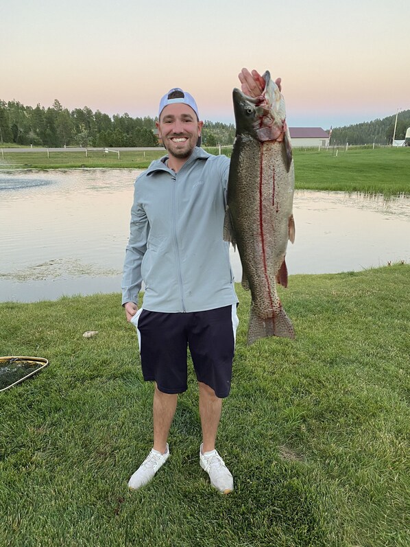 A person holding a large fish on a grassy area near a body of water.