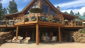 Une cabane en rondins dotée d’un balcon, d’un espace extérieur aménagé et d’une façade en pierre.