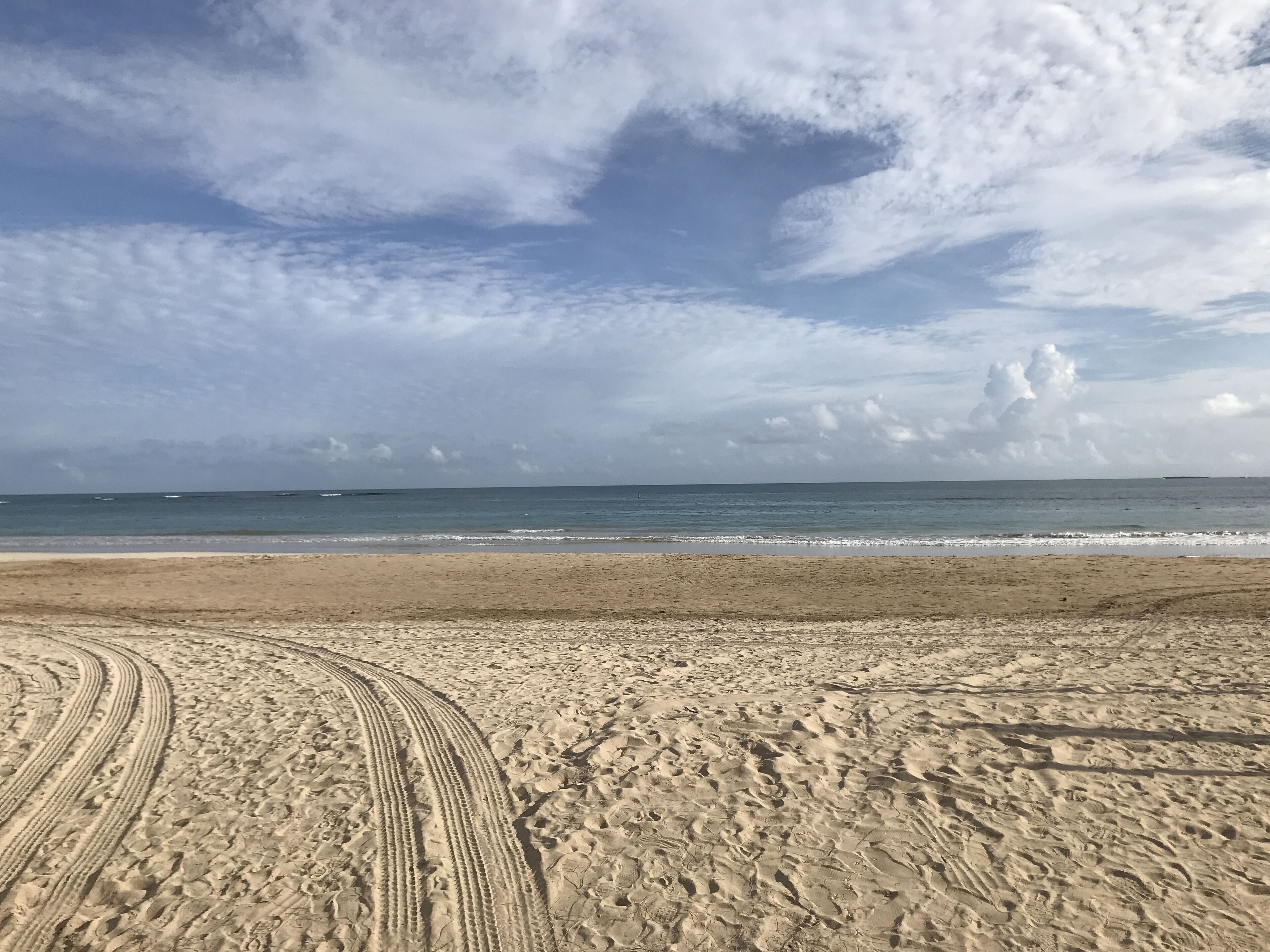 Ein sandiger Strand mit Radspuren, die zum Wasser führen.
