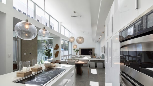 A modern kitchen with a central island, stainless steel appliances, pendant lighting, and large windows allowing natural light.