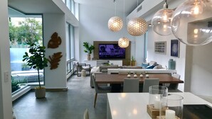 A modern living room with a large TV, comfortable seating, and a dining area with a glass table.
