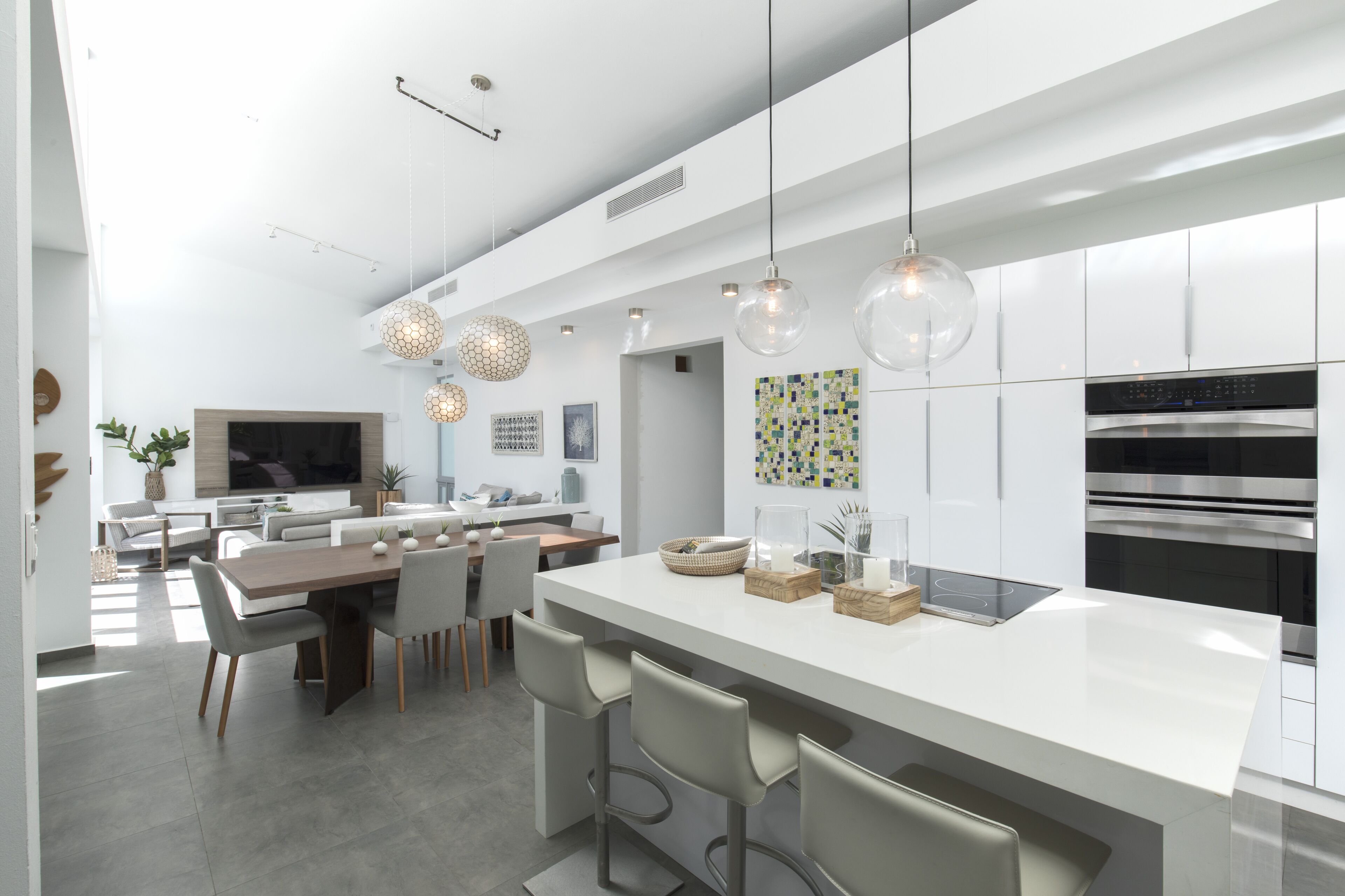 Ett modernt kök med en central köksö, barstolar, hängande lampor och en stor ugn.