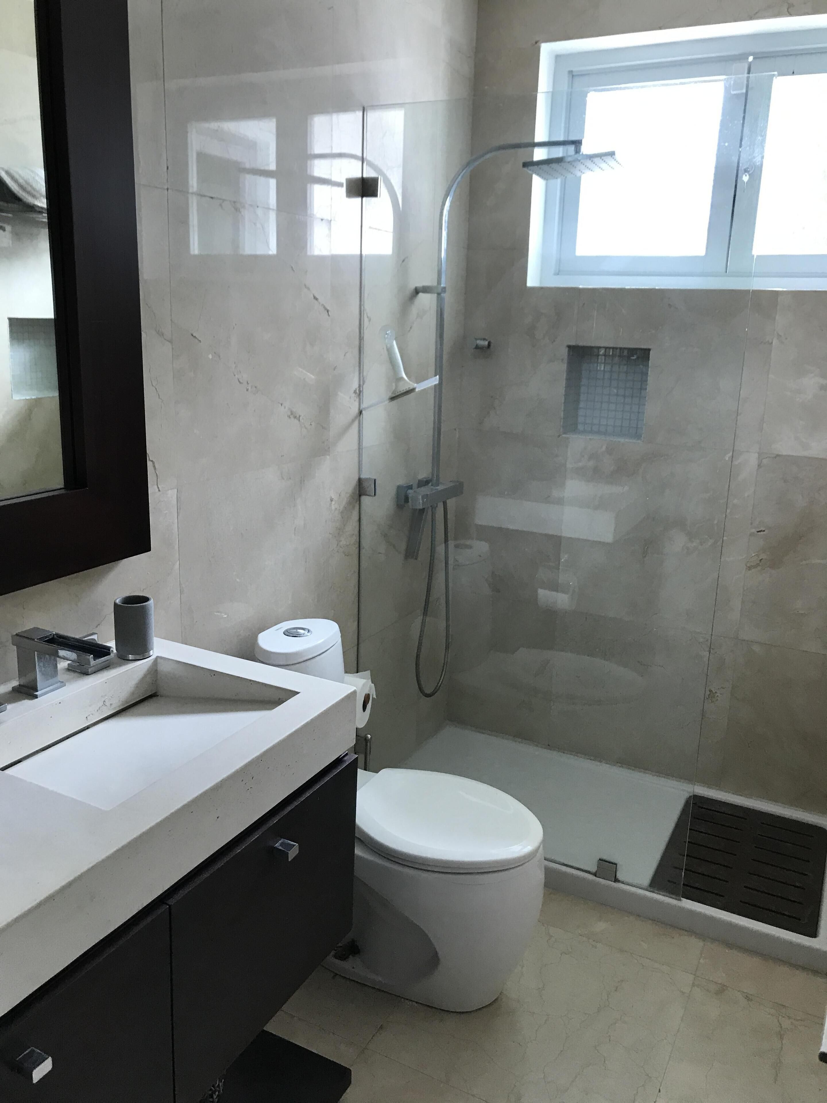 Un baño con inodoro, lavamanos, espejo, ducha y ventana.