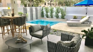 A poolside area with wicker furniture, a small table, and a blue umbrella.