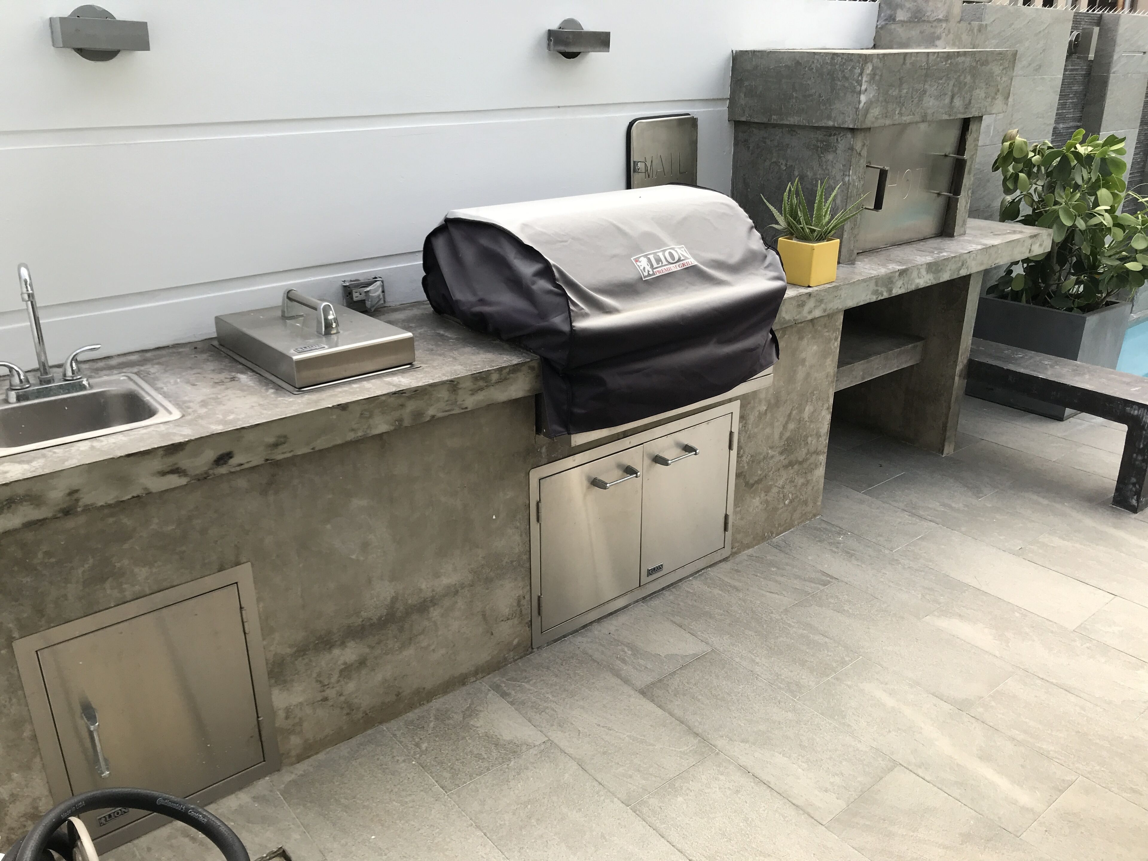 Una cocina al aire libre con pileta, una cubierta para la parrilla y una jardinera con plantas verdes.