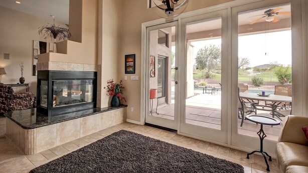 Un salon spacieux doté d’une cheminée, d’une grande porte vitrée donnant sur une terrasse extérieure et d’un ventilateur de plafond.