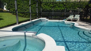 Une piscine avec un jacuzzi, entourée d’un espace couvert aménagé avec des chaises.