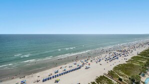 Une plage bordée de rangées de parasols et de chaises longues, un ciel dégagé et l’océan.