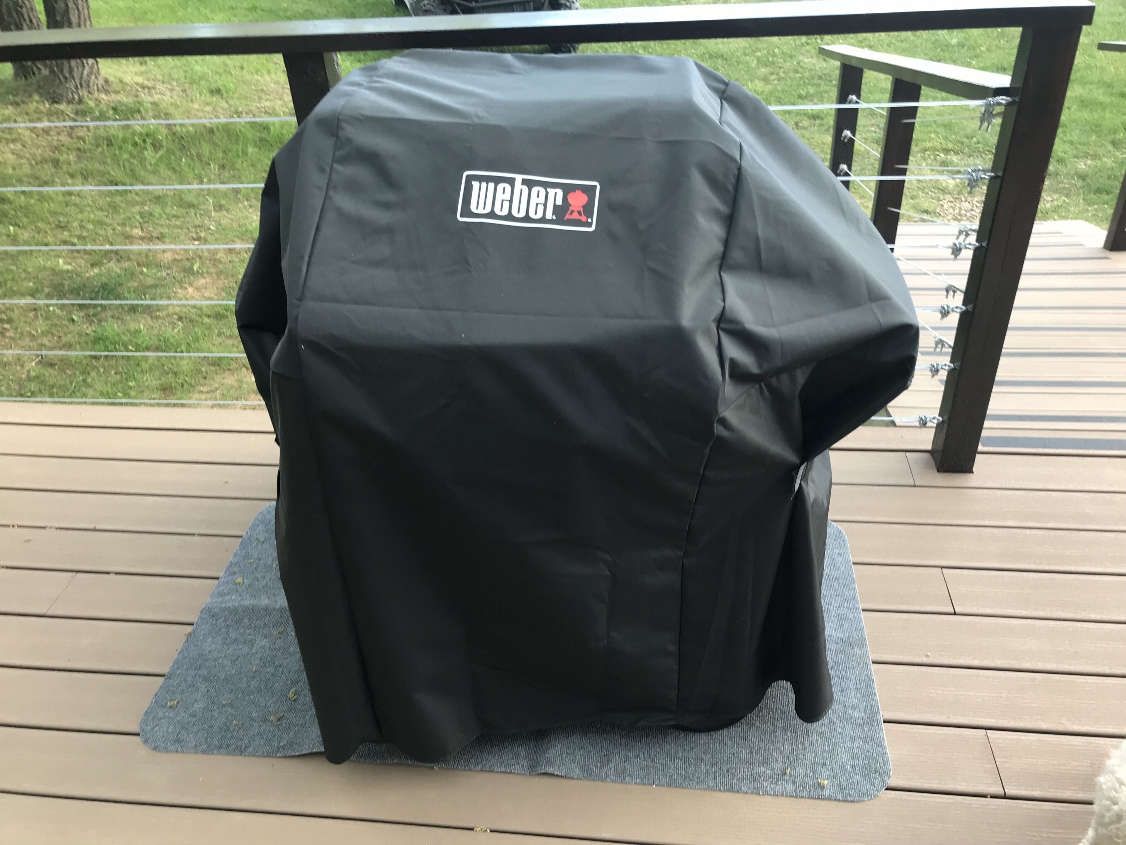 Een Weber barbecue op een houten terras, met een metalen hekwerk op de achtergrond.