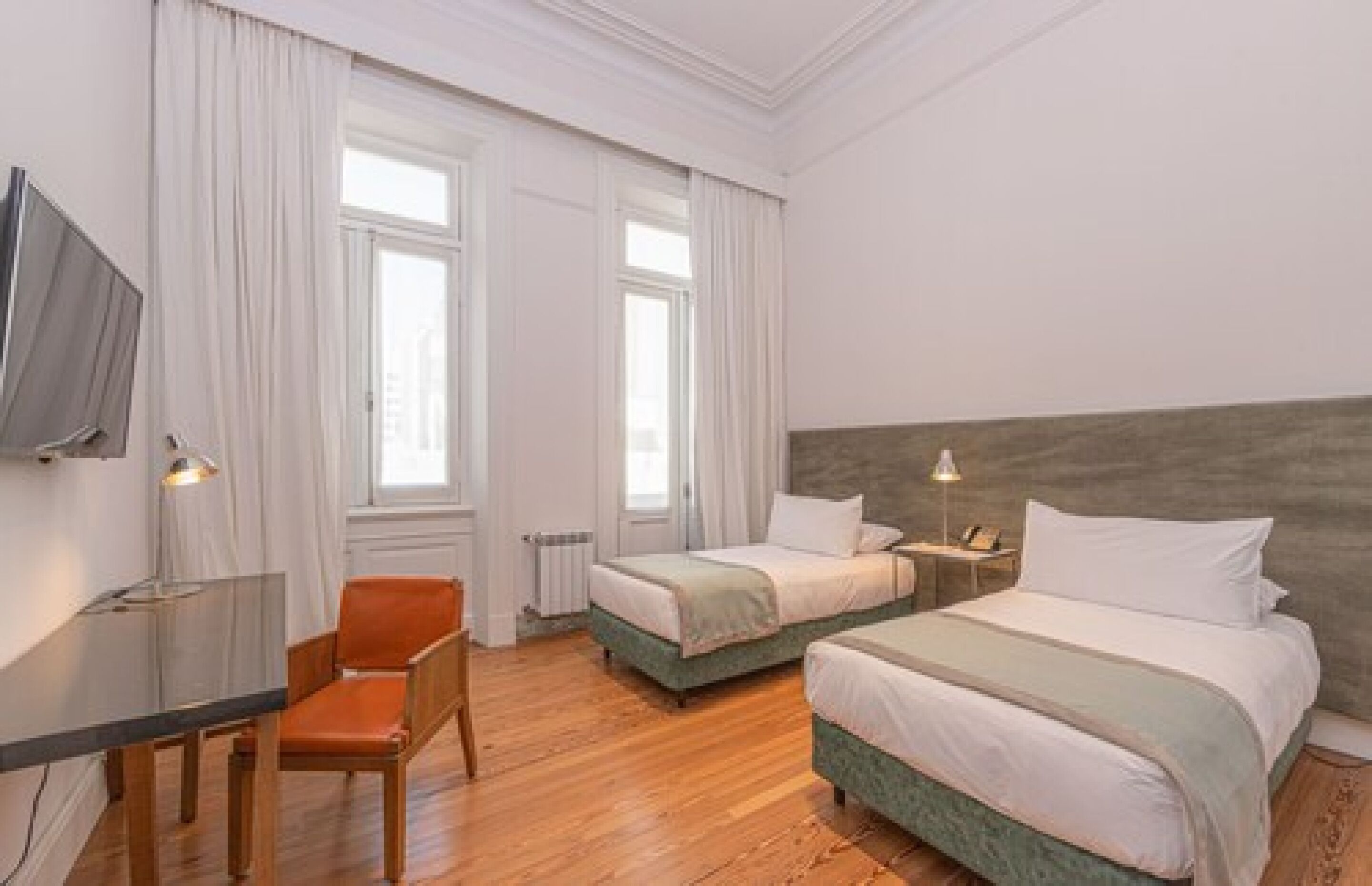 Quarto de hotel com duas camas, uma escrivaninha, uma cadeira e uma televisão.