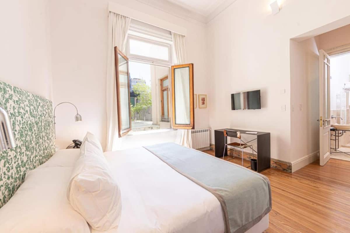 Habitación de hotel con una cama grande, un escritorio, un televisor y vistas al exterior.