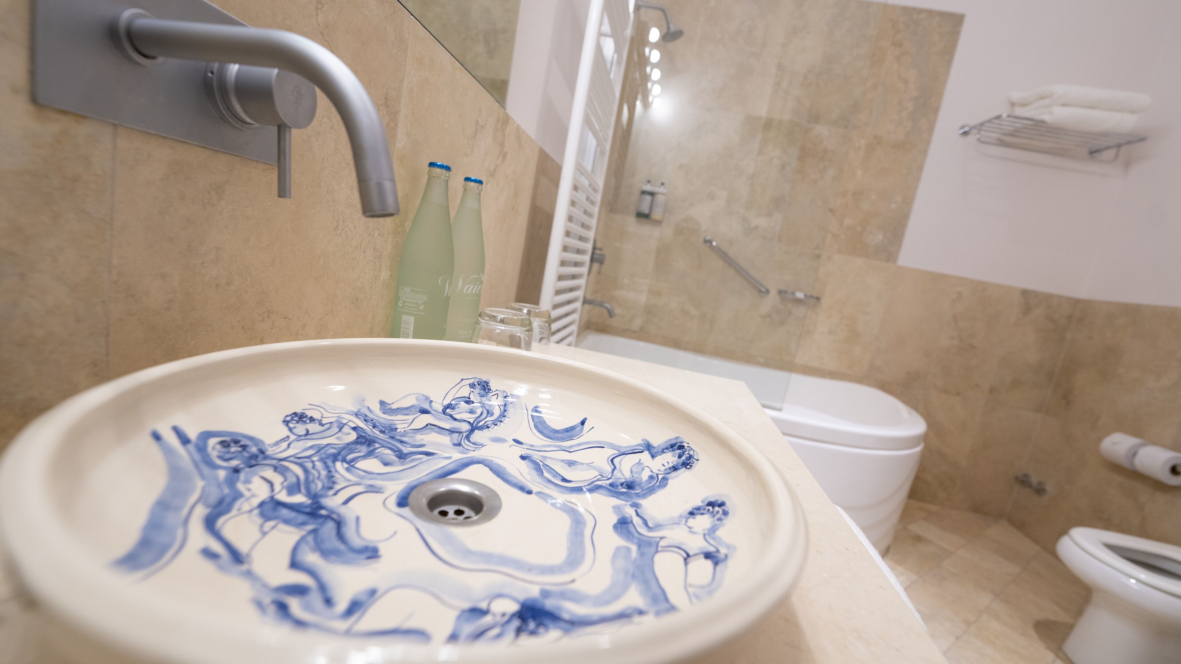 Un baño con un lavabo blanco con motivos florales azules, un inodoro blanco y una zona de ducha.