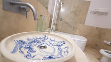 Un baño con un lavabo blanco con motivos florales azules, un inodoro blanco y una zona de ducha.