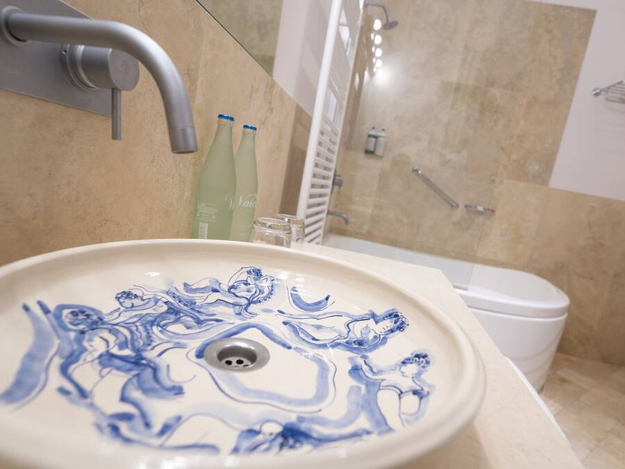 Un baño con un lavabo blanco con motivos florales azules, un inodoro blanco y una zona de ducha.
