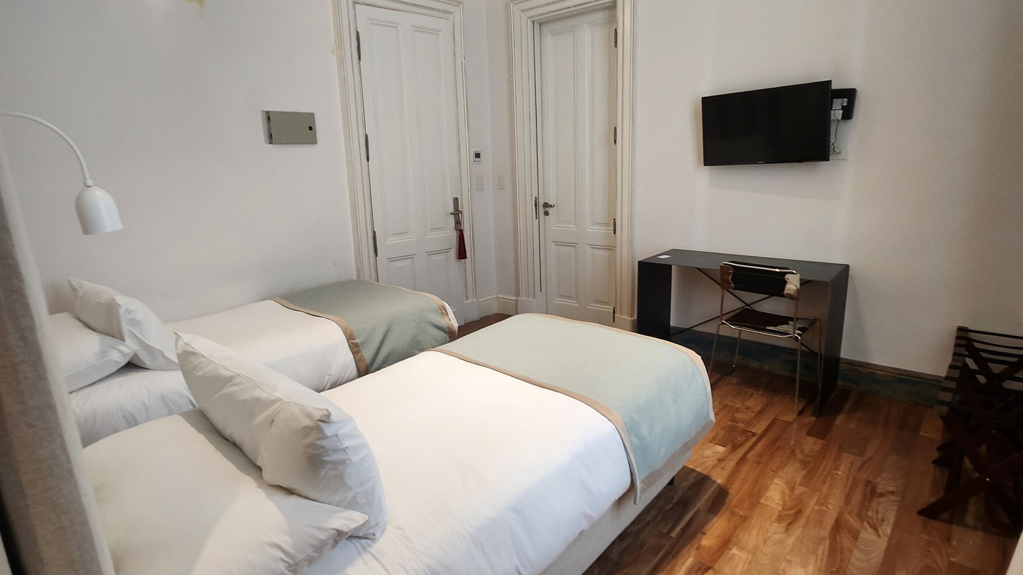 Una habitación con dos camas individuales, un escritorio con silla, un televisor de pantalla plana y piso de madera.
