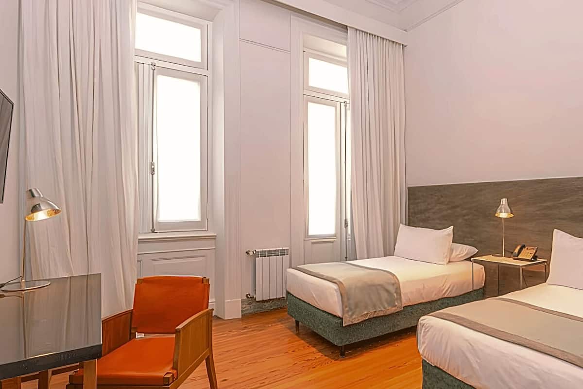 Habitación de hotel con dos camas, un escritorio, una silla y una mesita de noche con lámpara.